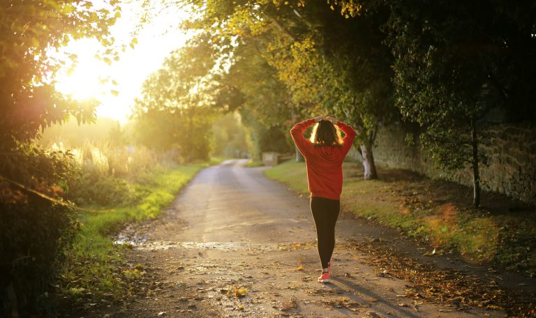 Un jeune fille qui marche sur un long chemin arboré et ensoleillé